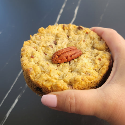 Hand holding a cookie with a pecan on top against a dark background